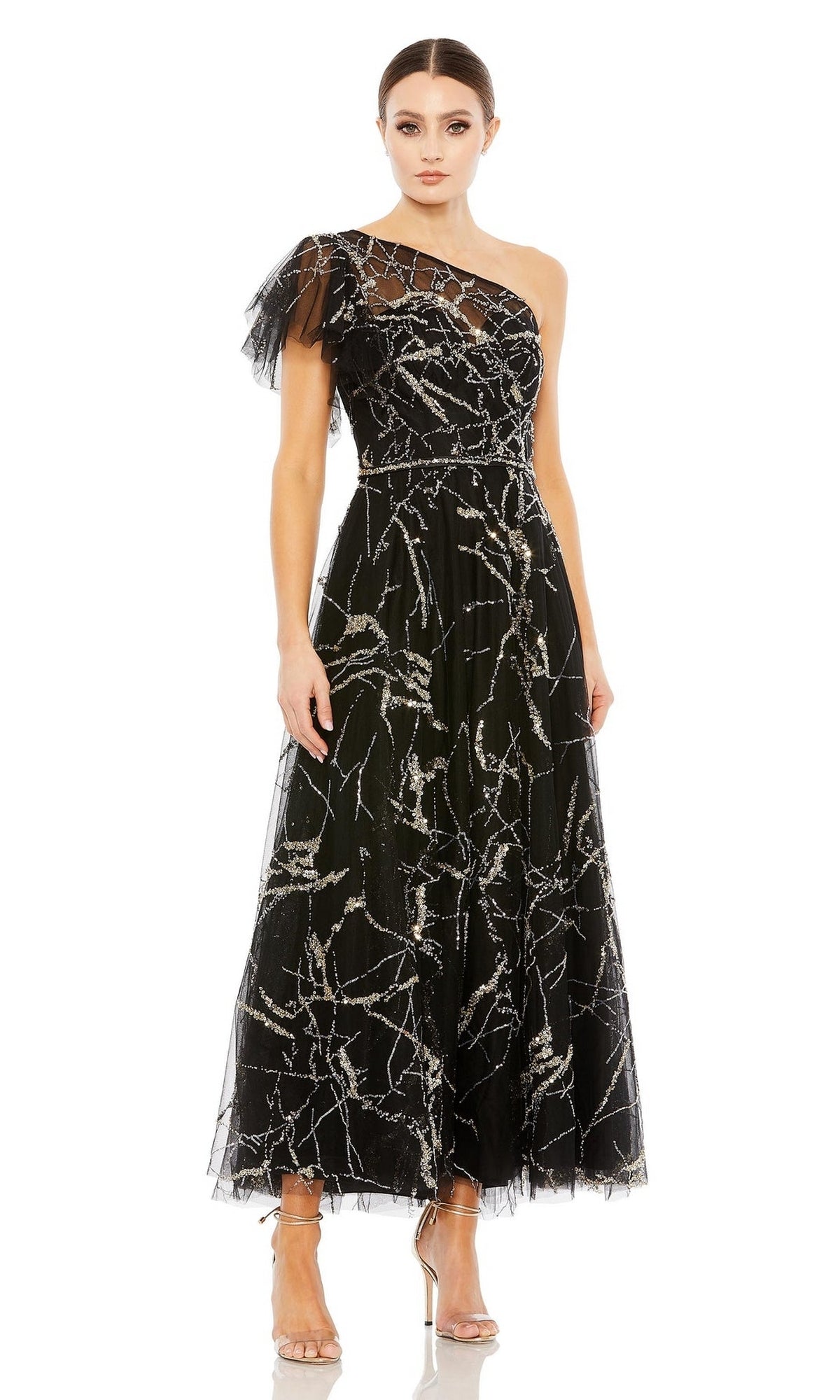 A woman wears the Long Formal Dress 20427 by Mac Duggal, a striking black one-shoulder, ankle-length gown with silver sequins and tulle details, elegantly paired with clear high heels.